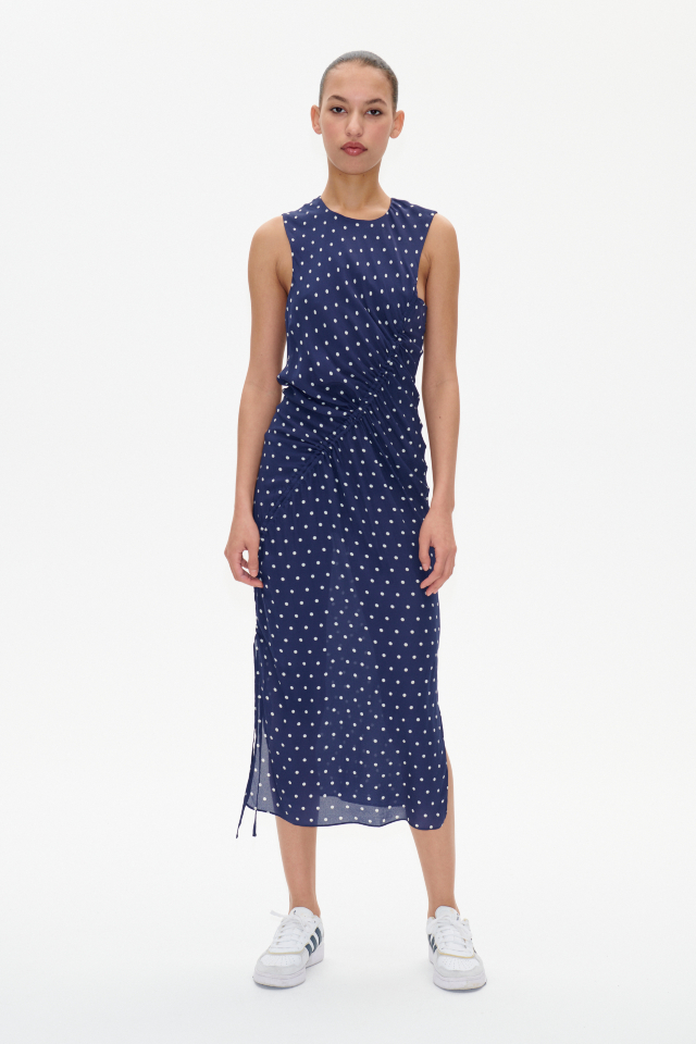 Allanna Dress Blue Margot Dot This midi-length, sleeveless dress features a button closure with keyhole opening in the back and ruching with an asymmetrical drawstring across the front - model image
